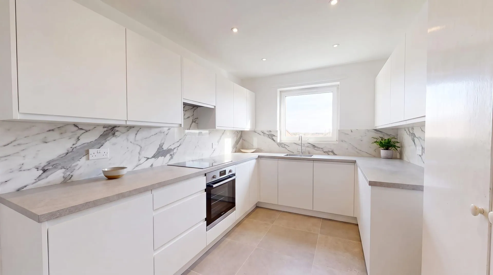 The same kitchen with a single white marble slab backsplash with bold grey veining and no grout lines