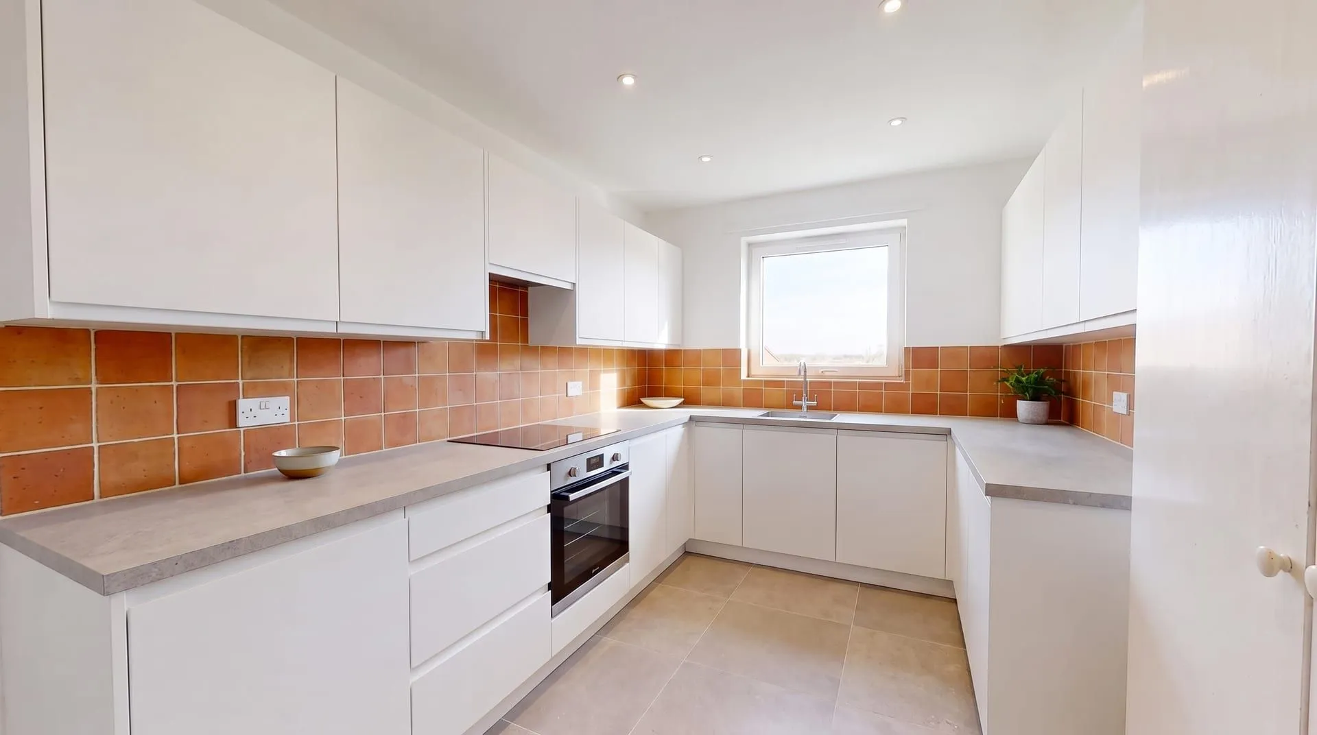 The same kitchen with a matte terracotta tile backsplash in warm orange-red squares with cream grout