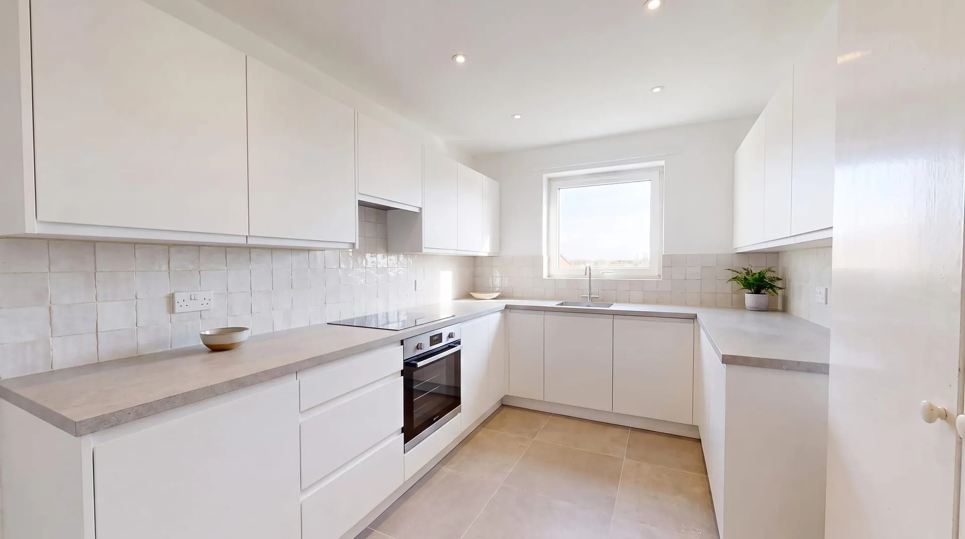 The sample kitchen with a white handmade zellige tile backsplash between the grey countertop and the white wall cabinets