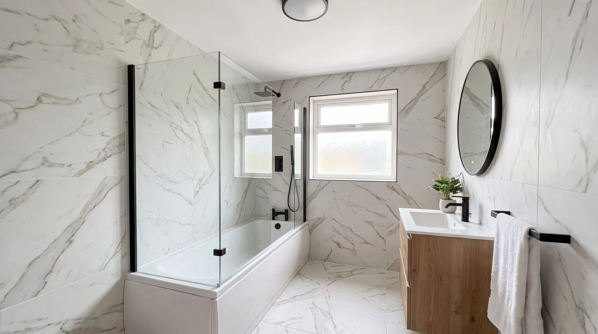 The sample bathroom tiled in large-format white marble-look porcelain on walls and floor, with a white bath, glass screen and oak vanity