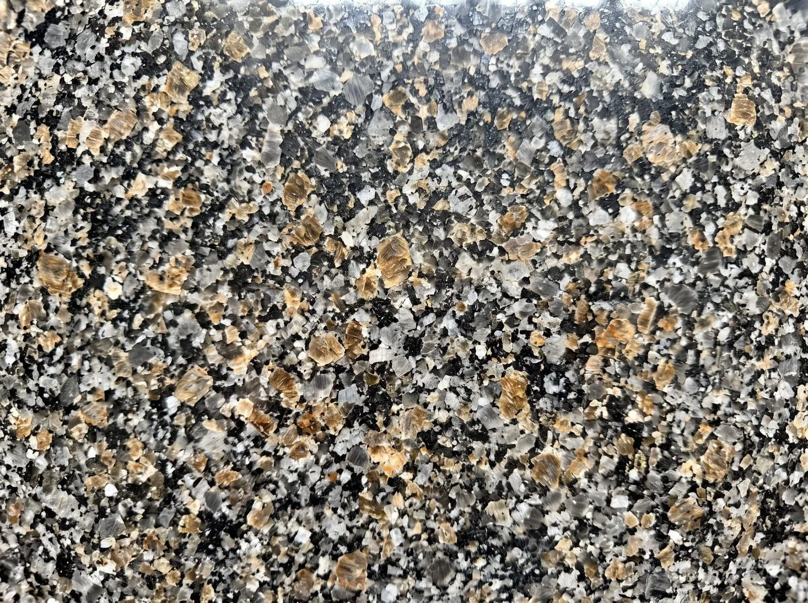 A close-up of polished granite showing a granular pattern of black, grey, white and amber mineral grains