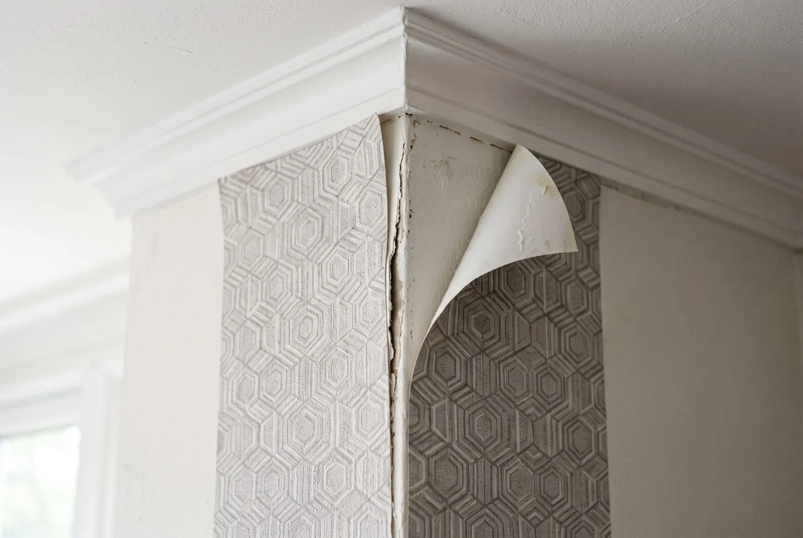 A close-up of peel and stick wallpaper at a wall corner where the seam has opened and one top corner has curled away
