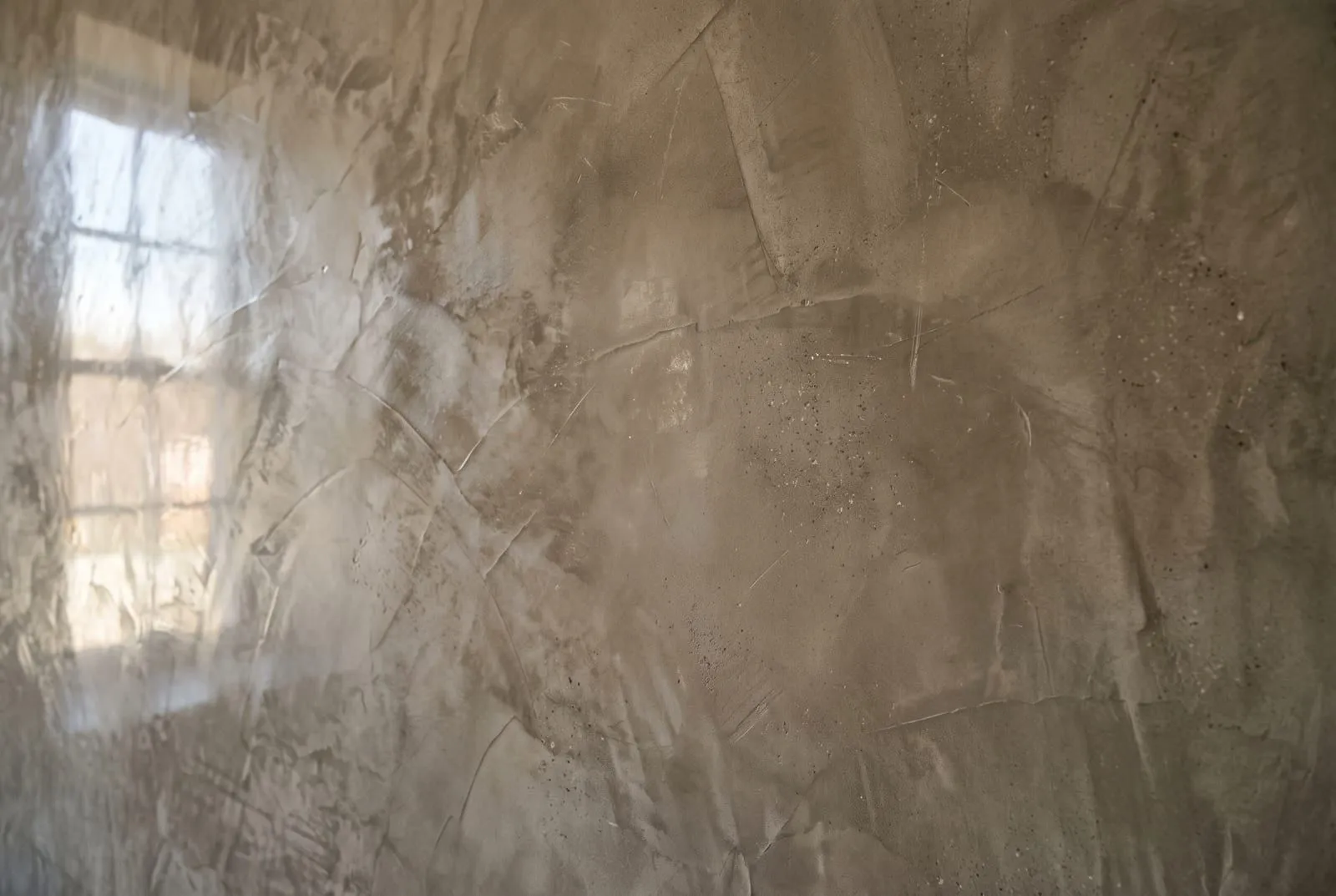 A close-up of polished Venetian plaster with layered trowel marks and a satin reflection of a window
