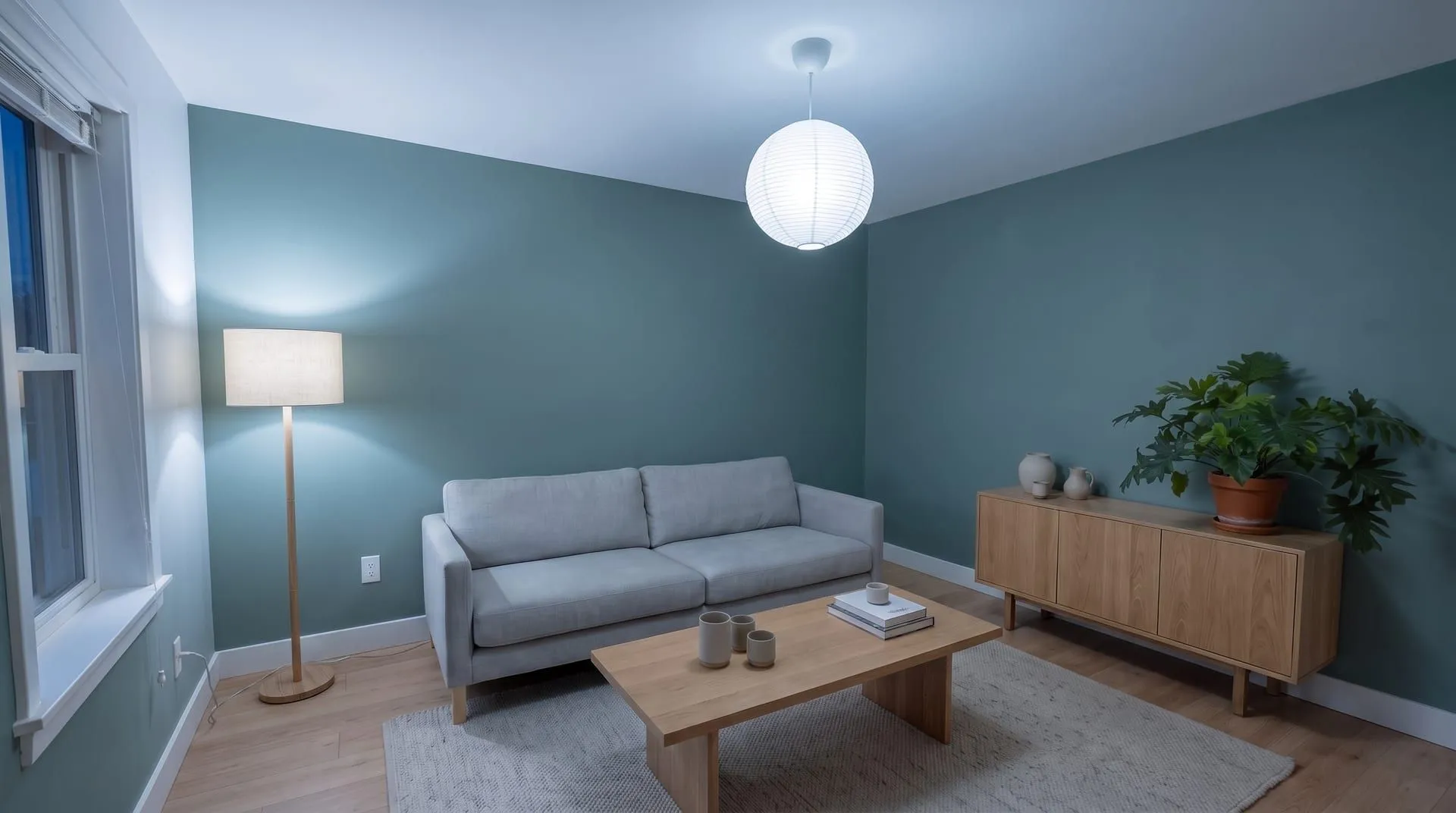 The same sage green living room at night under cool 5000K light, the walls looking blue-grey