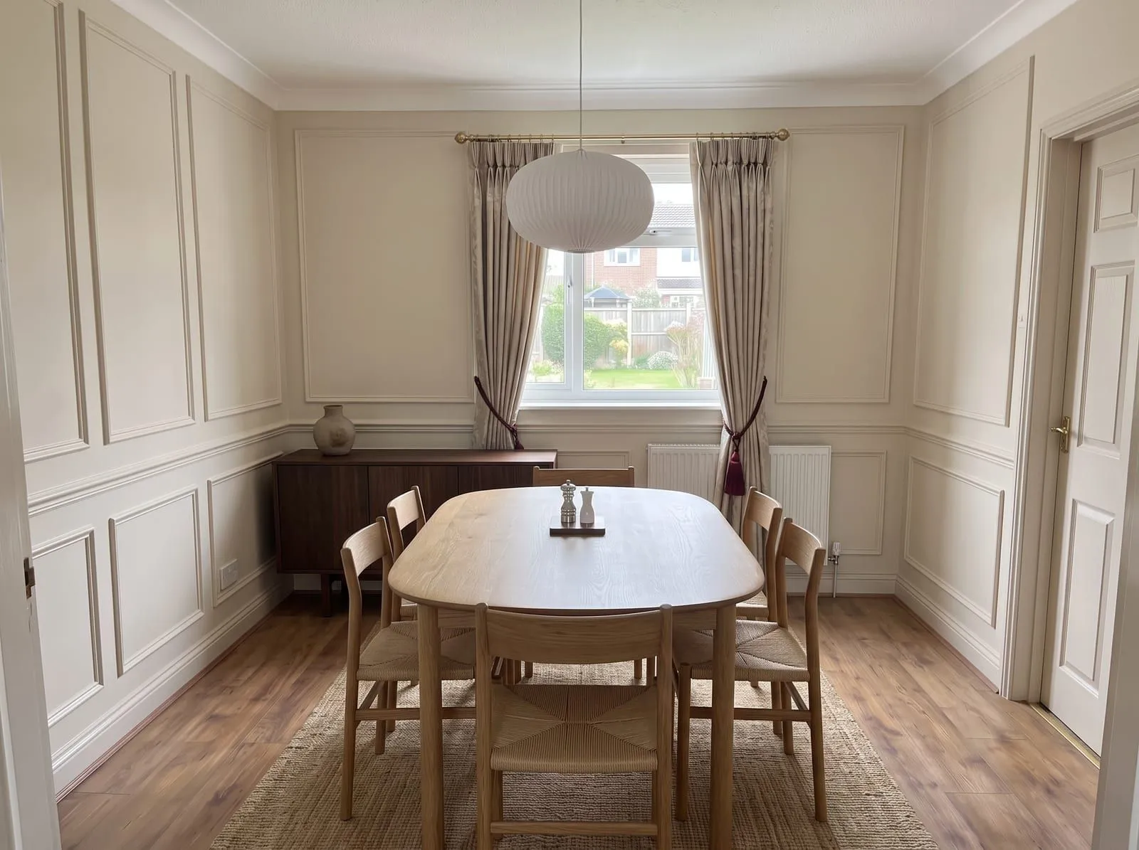 The sample dining room in Japandi style with a rounded oak table, woven seat chairs, a low paper pendant and a dark walnut sideboard