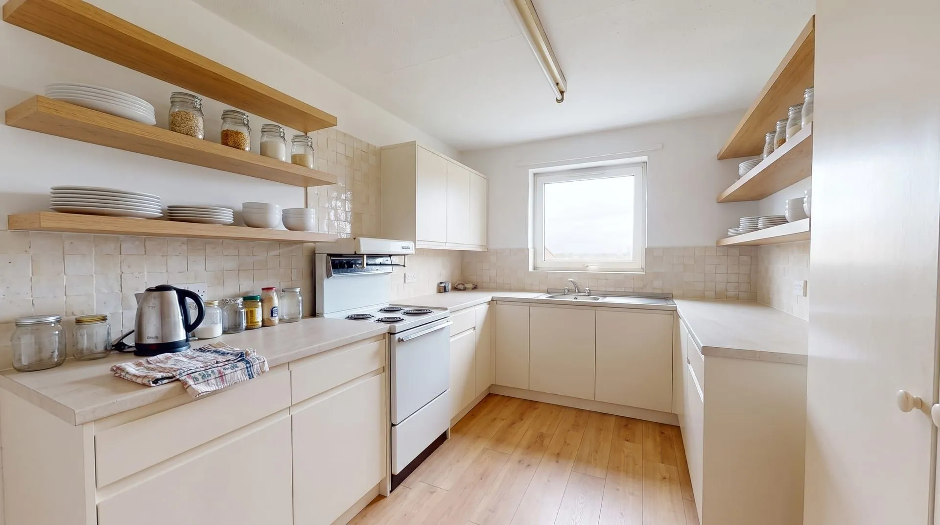 The same small kitchen redesigned with open oak shelves and a cream tile splashback