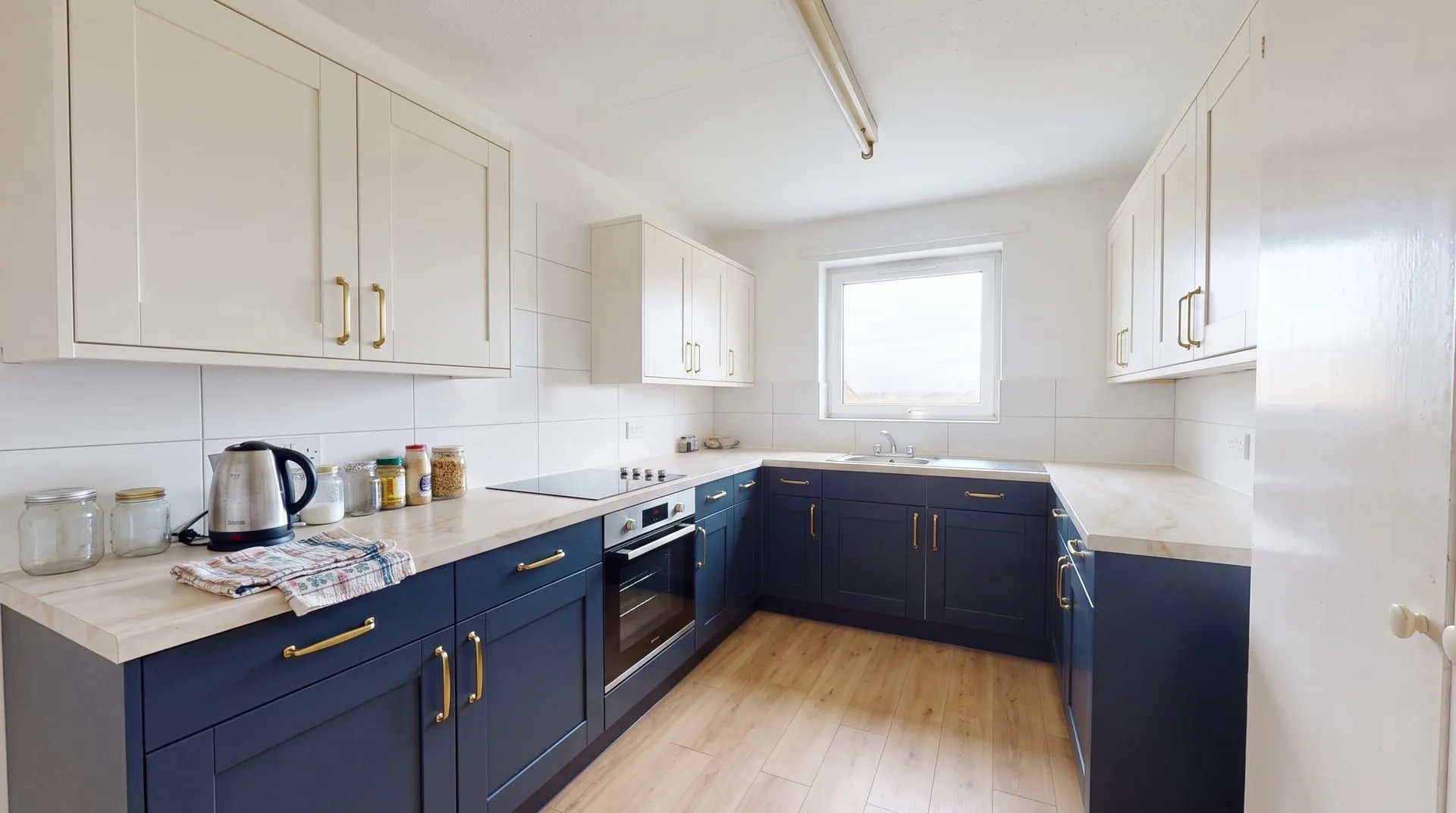 The same small kitchen redesigned with navy lower cabinets and warm white wall units