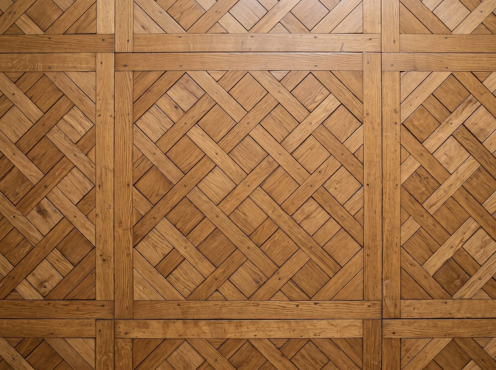 A top-down view of a Versailles oak parquet panel: a square border with a woven diagonal lattice inside