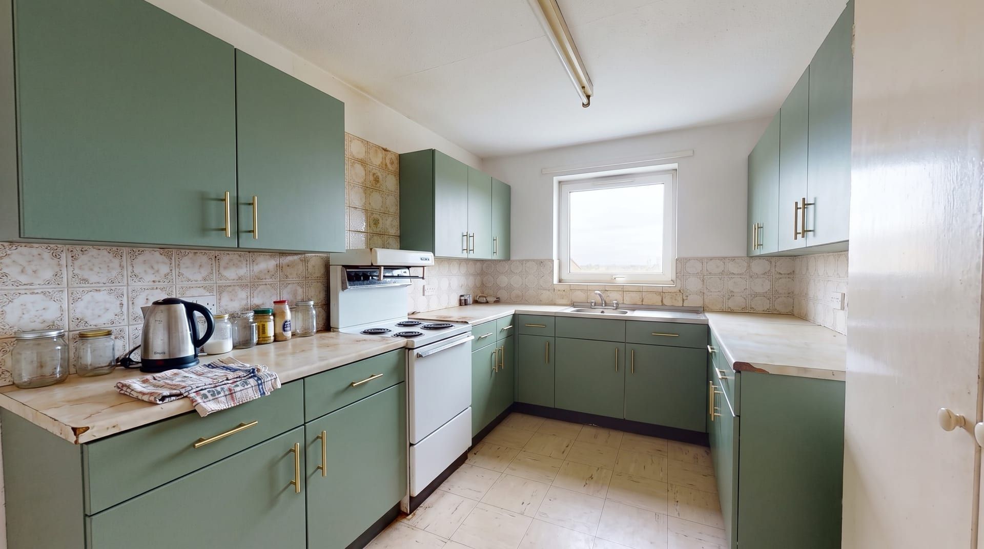 The same kitchen redesigned in a Sage green style, with its windows, walls and camera angle unchanged