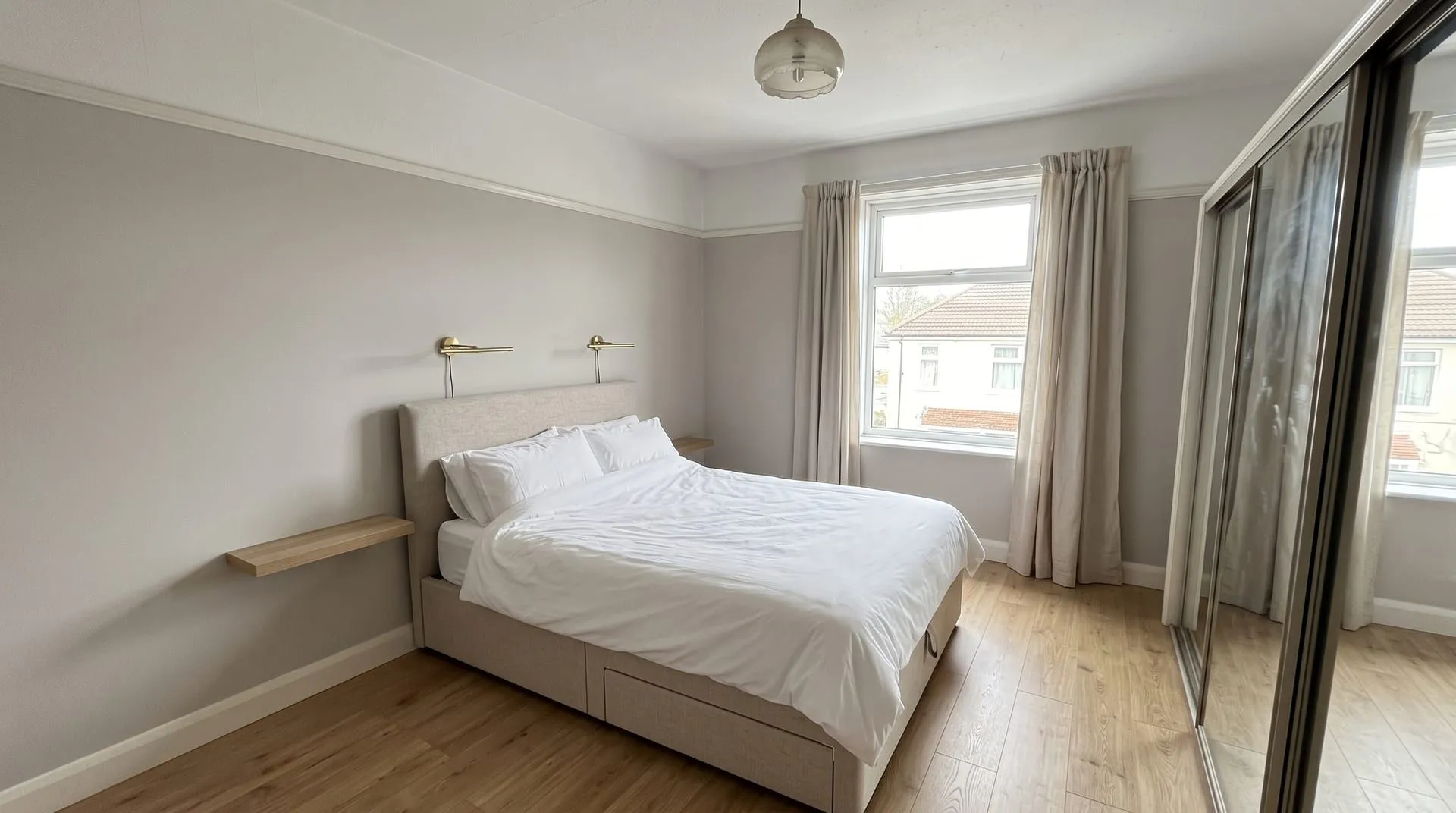 The sample double bedroom redesigned in a contemporary style with an upholstered storage bed, wall-mounted brass lights and a floating shelf