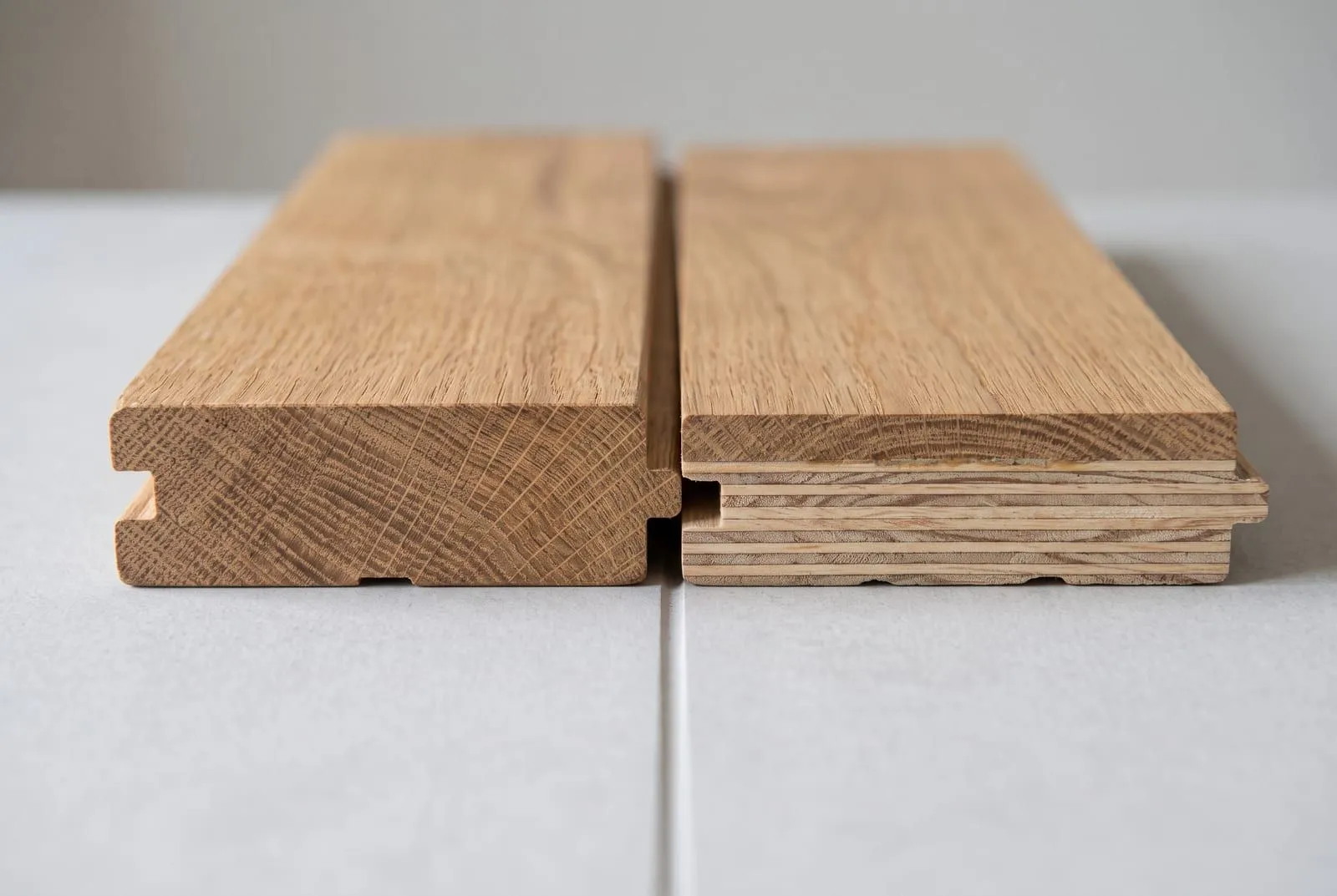 Two oak parquet blocks cut open side by side: a solid oak block on the left and an engineered block with an oak top layer on plywood on the right