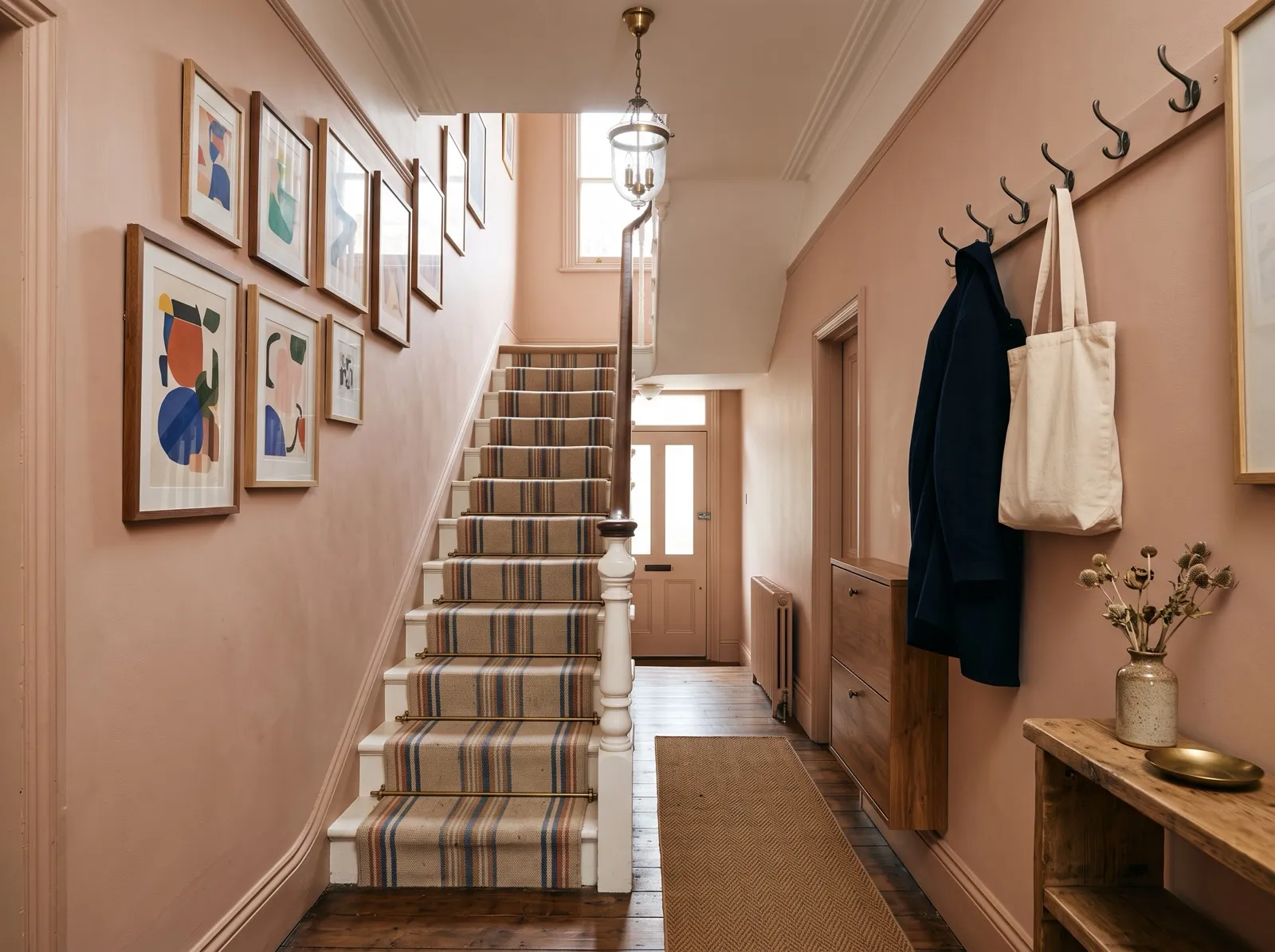 A stair hallway with a gallery of framed prints along the stairs, hooks, a wall-hung shoe cabinet and a runner